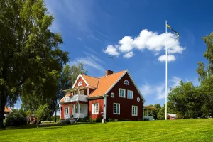 Rood houten huis met witte kozijnen naast een vlaggenmast met de Zweedse vlag op een groen grasveld
